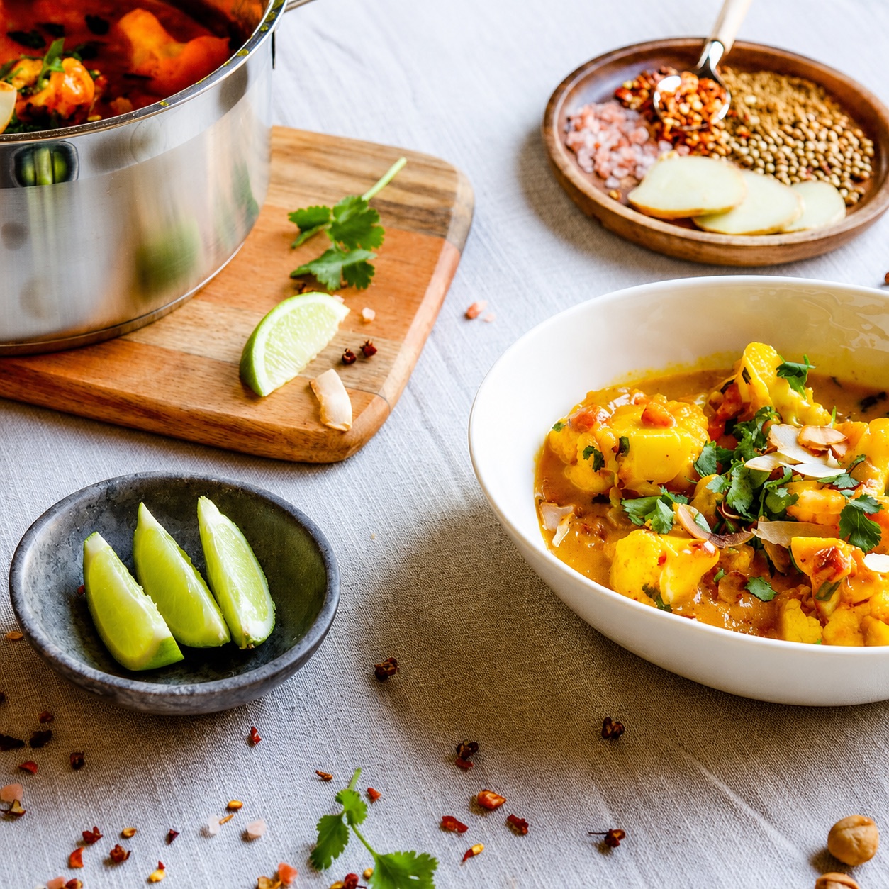 Cauliflower and macadamia curry in a white bowl with coriander, lime wedges and whole spices.