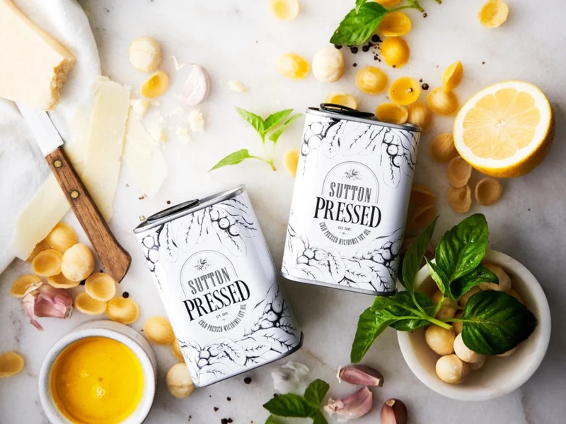Overhead flat lay of Sutton Pressed macadamia oil tins with pasta, parmesan, lemon and basil.